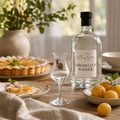 Weingut Sieferle Mirabellenwasser als edler Digestif auf warm gedecktem Holztisch mit Schnapsglas, Mirabellen, Obsttarte und natürlichen Materialien im Tageslicht.