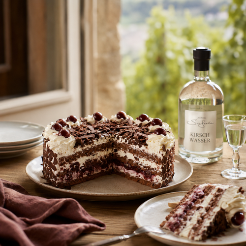 Schwarzwälder Kirschtorte auf rustikalem Tisch mit Kirschwasser BIO-Qualität von Genusswelt Sieferle im Hintergrund